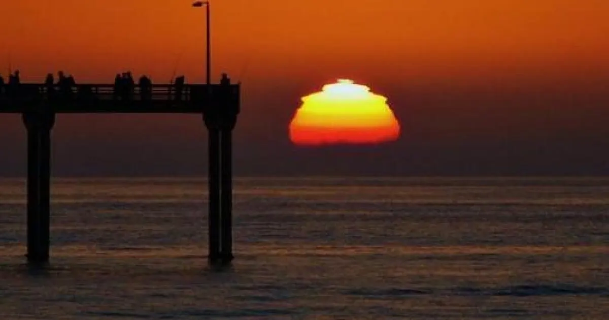 The sun flattening into the ocean beside a silhouetted San Diego pier at sunset