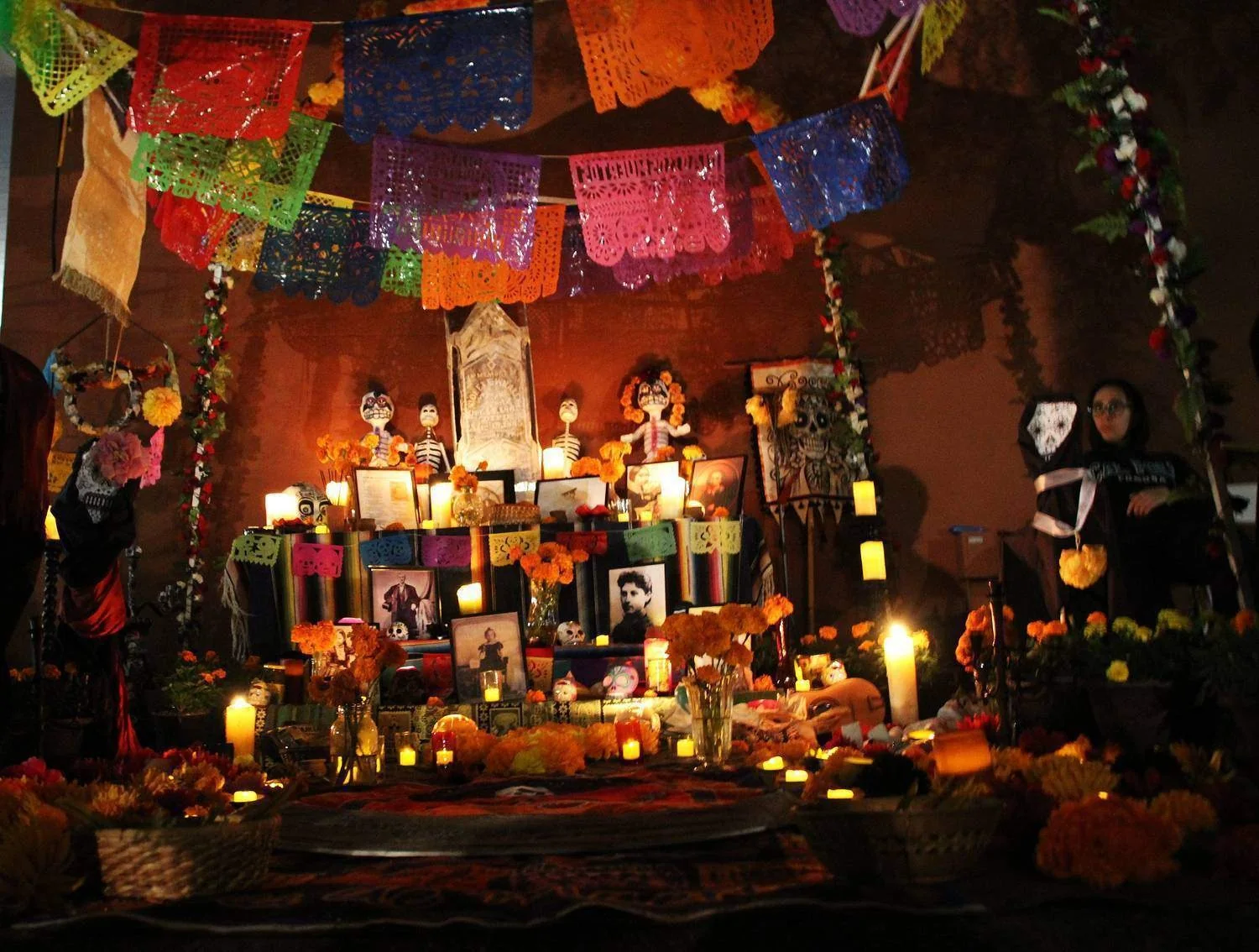 A Dia de los Muertos altar in Old Town at night, candles, marigolds, photos and papel picado strung overhead