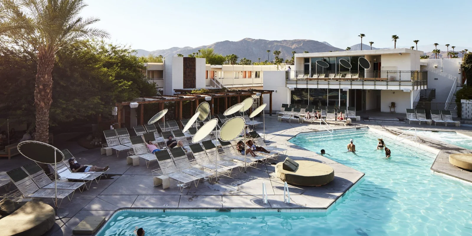The main pool at the Ace Hotel & Swim Club in Palm Springs, lounge chairs around the deck and the mountains behind the hotel