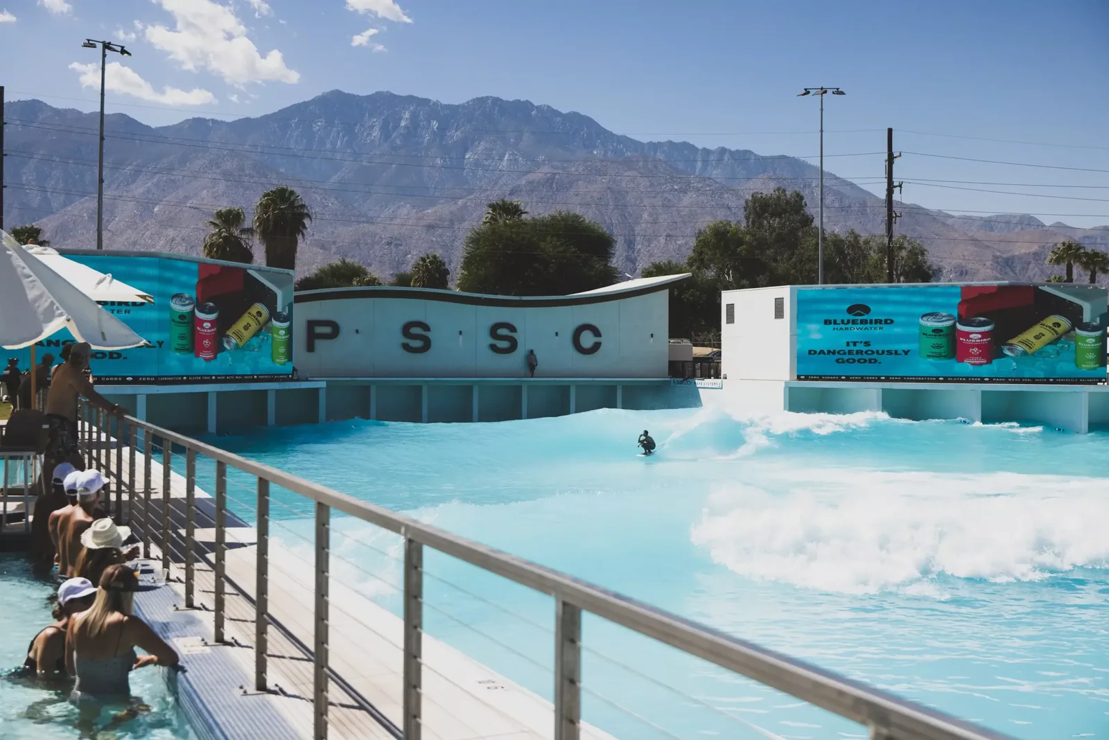 The wave pool at Palm Springs Surf Club, a surfer riding a wave in front of the PSSC wall with the mountains behind