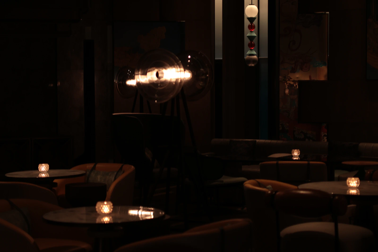 A dim hotel lounge bar, candles on every table and a glass lamp glowing over the leather chairs
