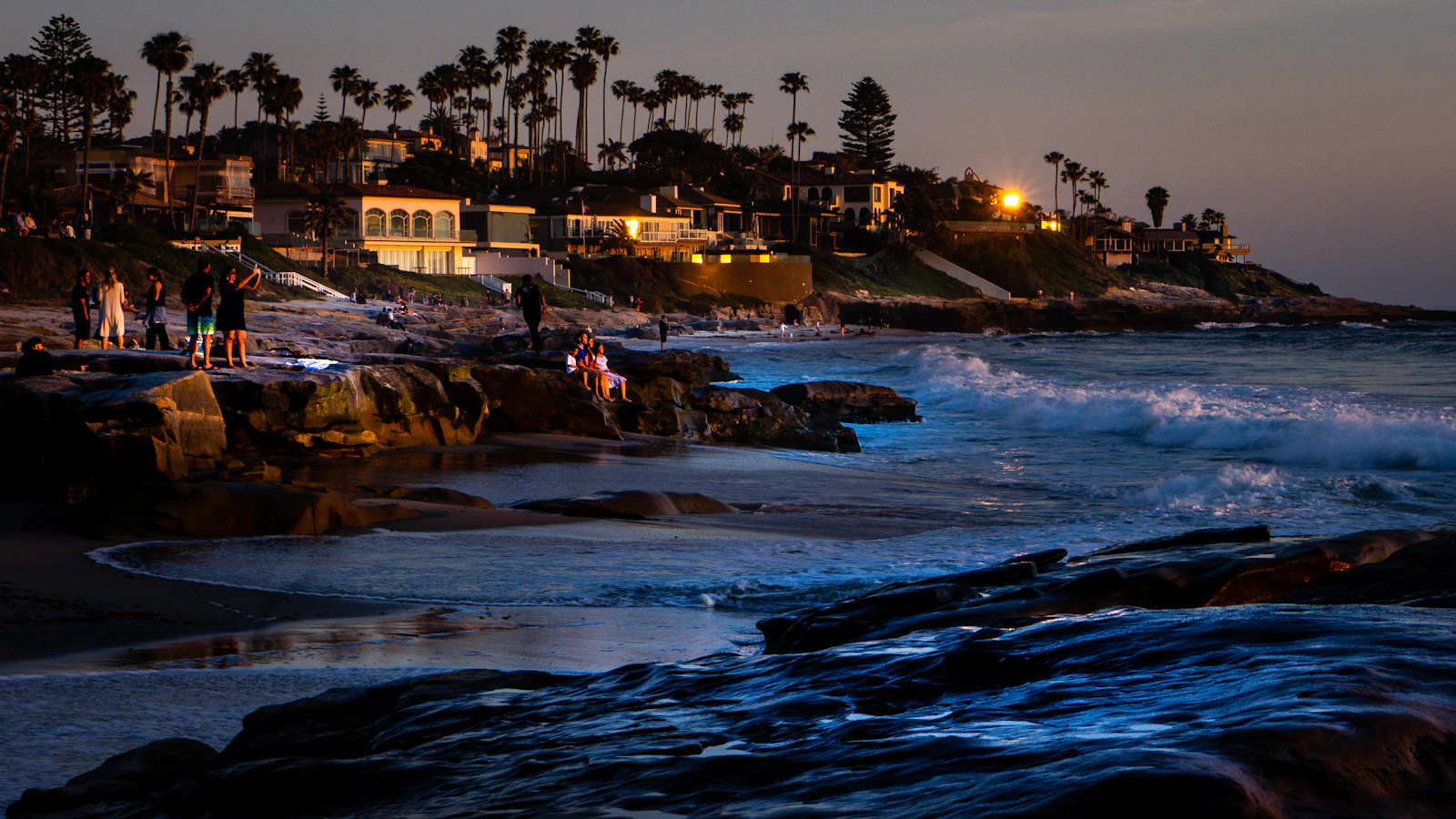 People out on the sandstone shelves at Windansea as the last light goes, houses lit up on the bluff behind