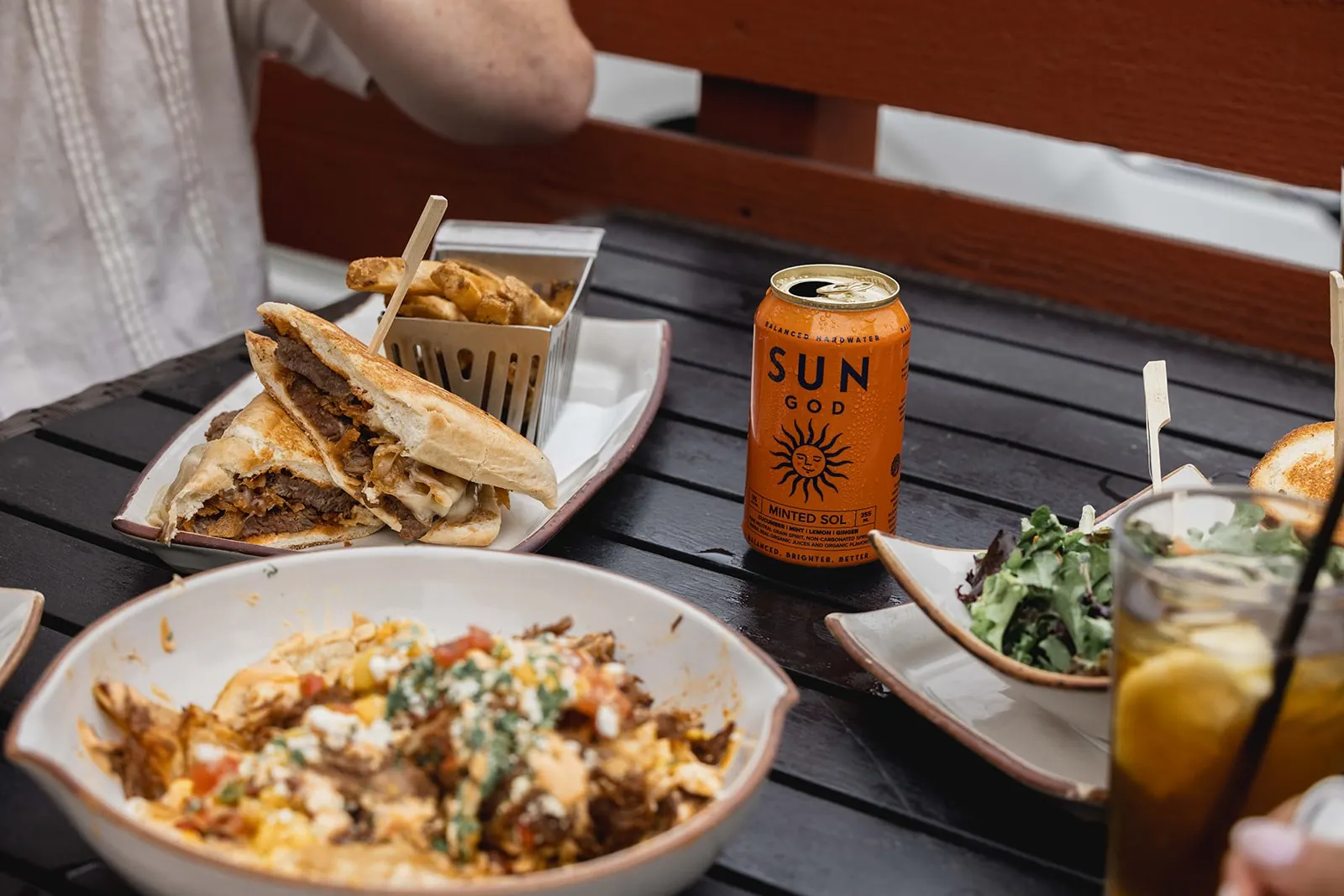 A Cardiff Crack steak sandwich and fries on a patio table next to a can of Minted Sol