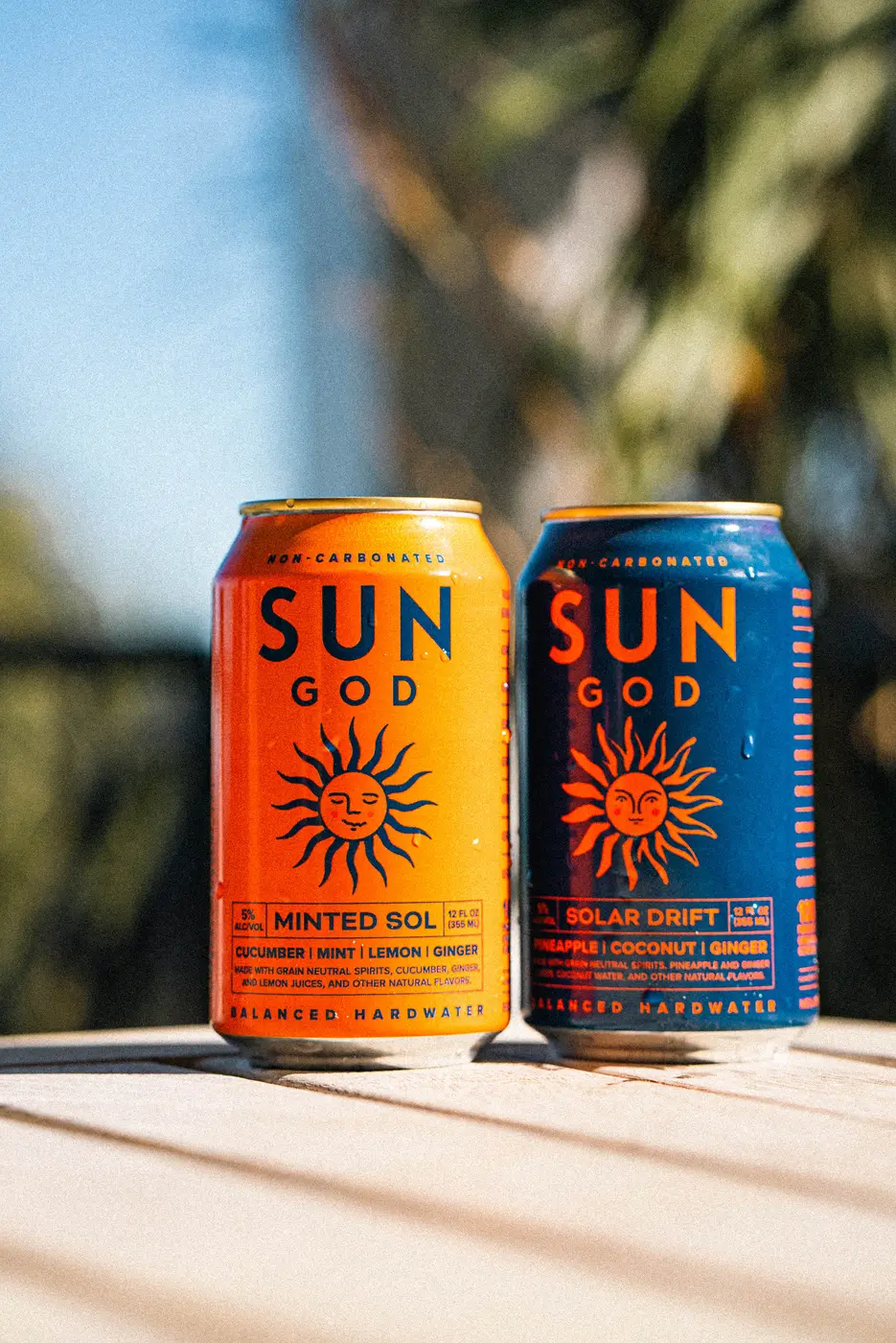A Minted Sol and a Solar Drift on a sunlit ledge, palm fronds blurred behind them